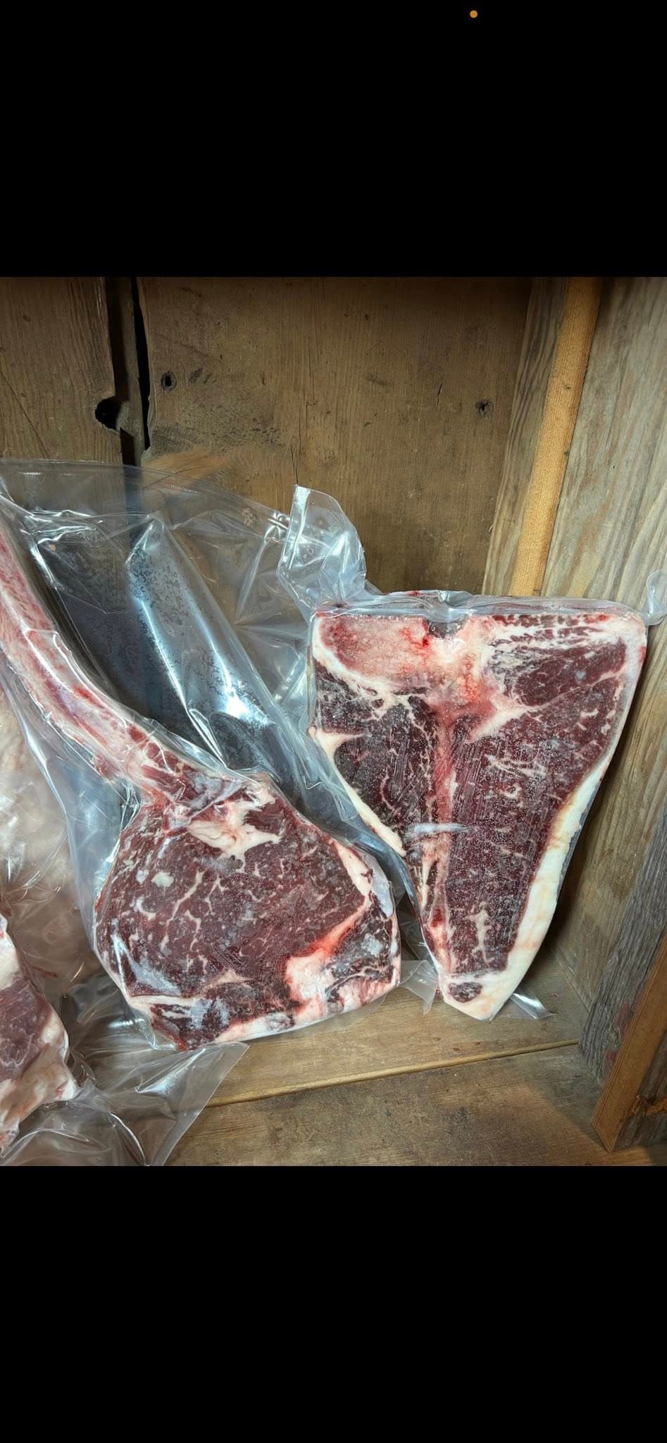 Vacuum-sealed tomahawk ribeye and T-bone steaks on a wood background