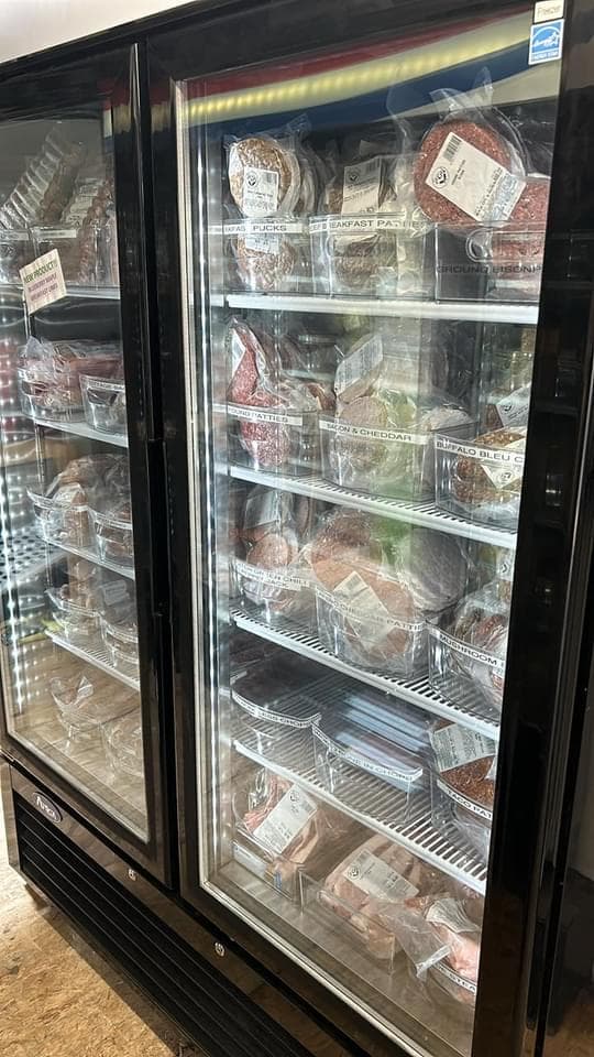 Retail freezer with labeled bins of burgers, brats, and specialty meats